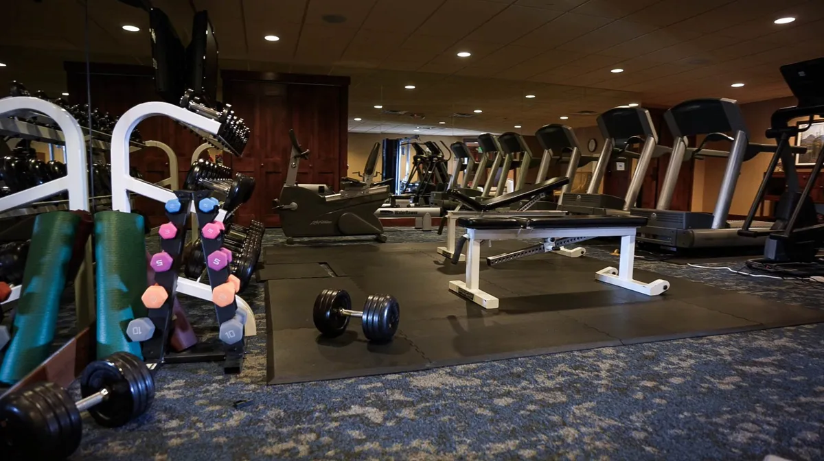 A bright, modern fitness center equipped with dumbbells, treadmills, a weight bench, and exercise mats. Guests are seen engaged in both solo and group fitness activities, emphasizing the social and active lifestyle available at the resort.