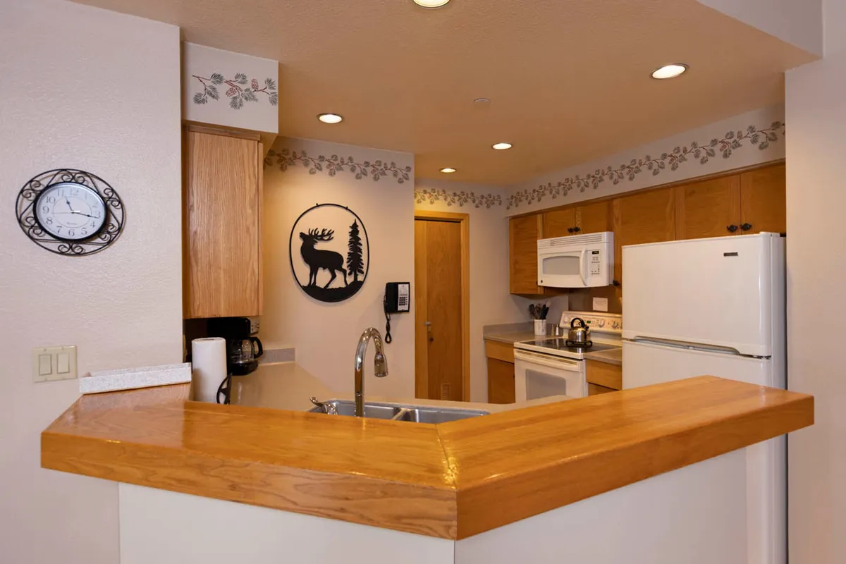 A bright, functional kitchen featuring a sizable kitchen island, reindeer wall art for a touch of alpine charm, visible modern appliances, and spacious counters. The arrangement suggests a space designed for both cooking and social connection, with décor that enhances the mountain getaway vibe.
