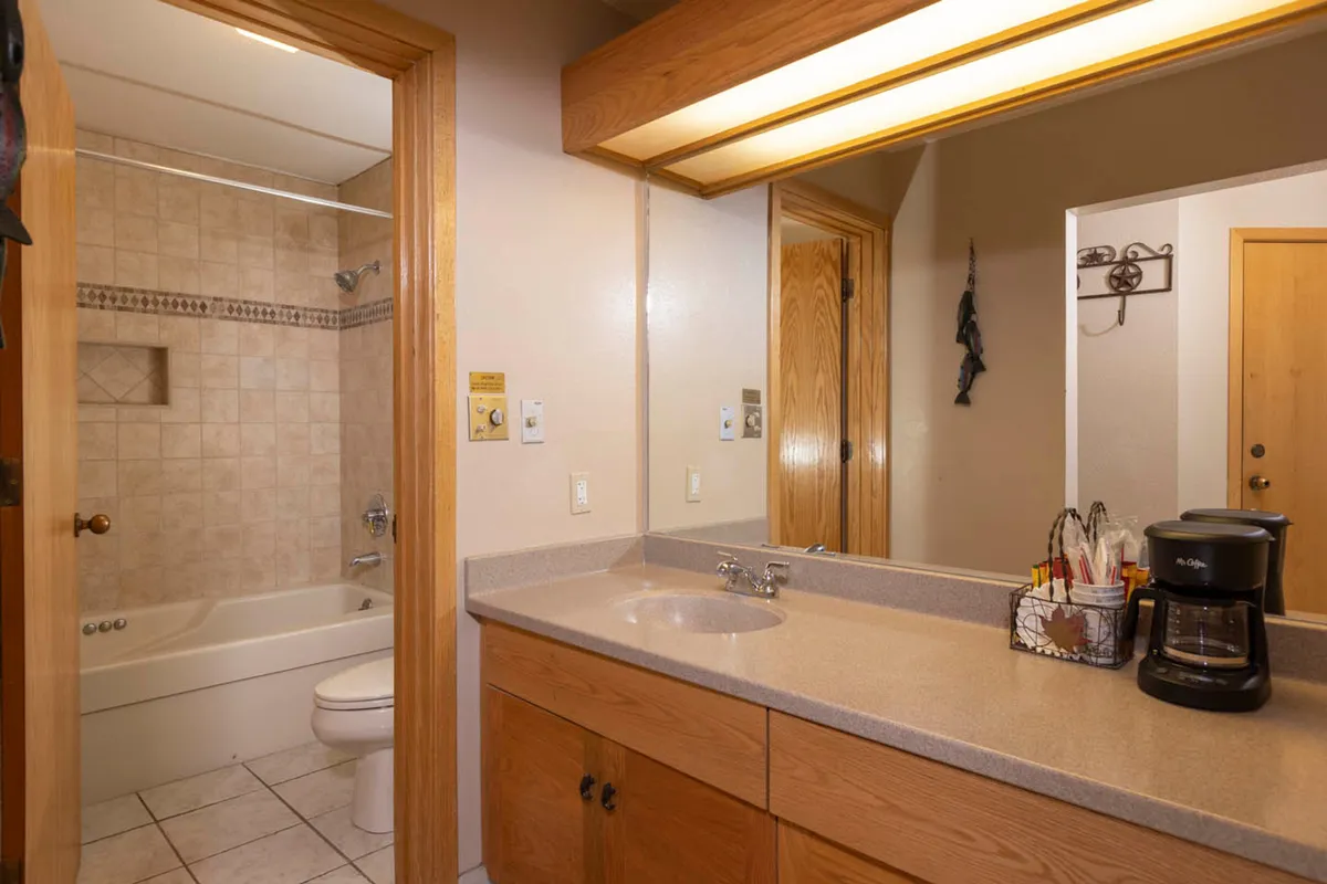 An inviting bathroom scene featuring a mirror, sink, bathtub, and coffee maker, designed for private relaxation. The setting evokes a sense of comfort and luxury, ideal for quiet moments spent together after a day outdoors.